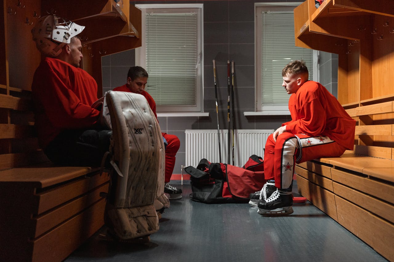 about-02 Three ice hockey players in a locker room wearing uniforms, getting ready for a game.